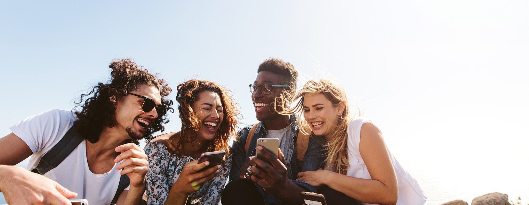 a group of friends sit outside laughing over their cell phones